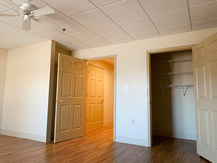 An empty room with hardwood flooring, featuring an open door, a closet, and a ceiling fan.
