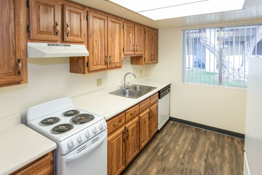 A compact kitchen with wooden cabinets, an electric stove, and laminate flooring.
