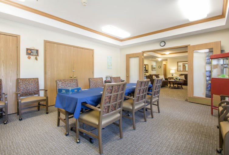 A spacious dining room with a blue tablecloth on the table and wooden chairs, featuring carpeted flooring and warm lighting.
