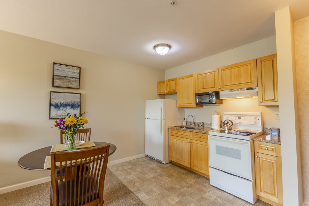 A cozy kitchen with wooden cabinets, featuring a dining set and floral centerpiece.