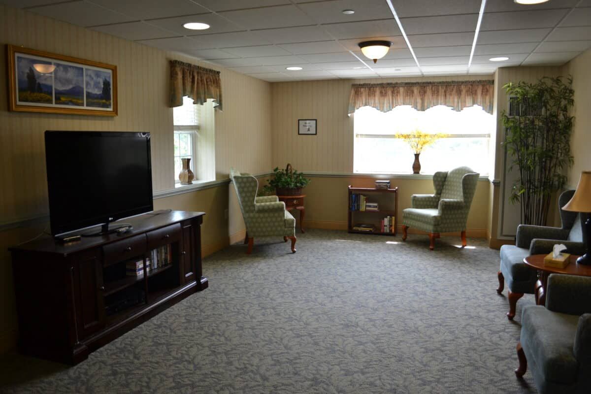 A cozy living room with a television, seating area, and large window.