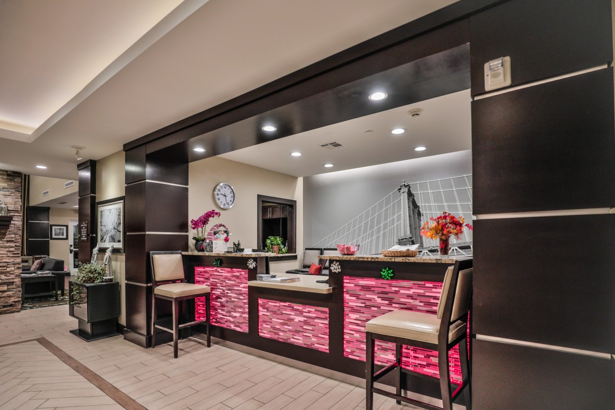 A modern reception area featuring a sleek desk with illuminated panels, comfortable chairs, and decorative floral arrangements.