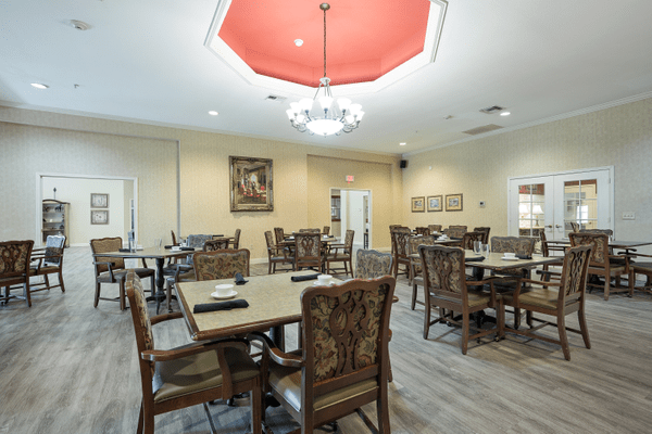 A well-decorated dining room featuring multiple tables and chairs under a central chandelier.