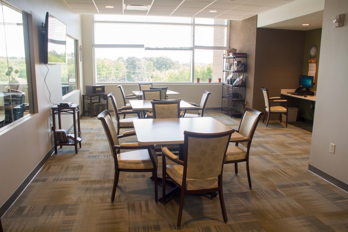 A modern dining area with tables and chairs, illuminated by natural light from large windows.