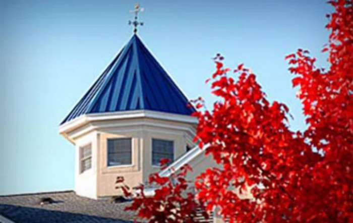 A building with a blue-roofed cupola and vibrant red autumn leaves in the foreground.