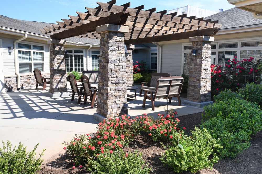 A beautiful outdoor pergola with stone columns, surrounded by a well-maintained garden and patio seating.