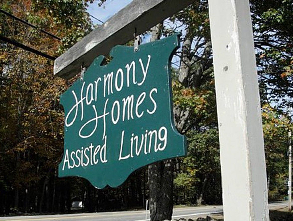 A wooden sign for Harmony Homes Assisted Living hanging outdoors.