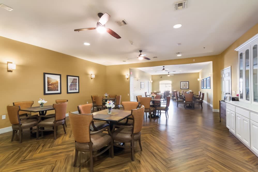 A spacious dining area featuring wooden floors, tables with comfortable chairs, ceiling fans, and decorative wall art.