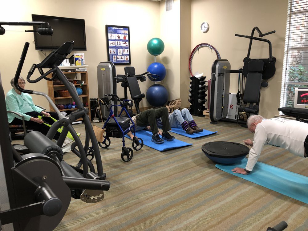 People exercising in a gym with various fitness equipment and yoga mats.