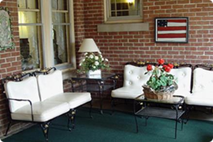 A cozy seating area featuring white upholstered furniture, a glass table, and decorative plants, complemented by an American flag wall art.