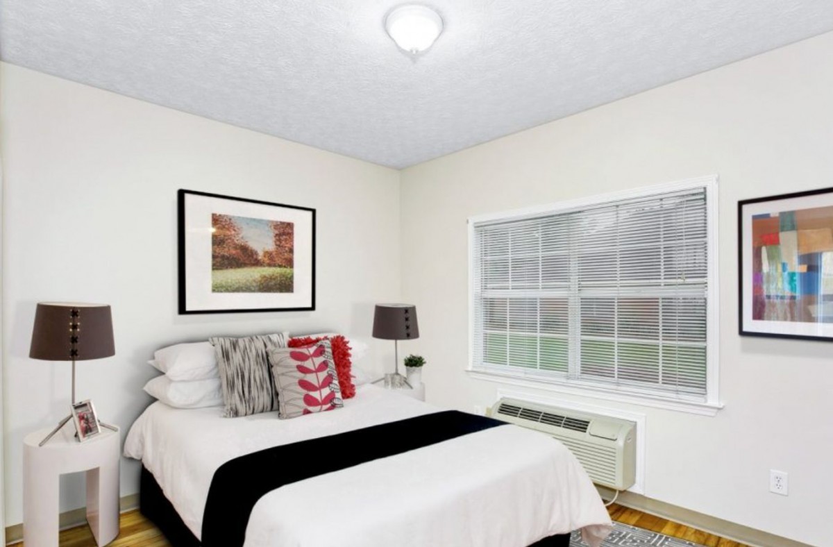 A cozy bedroom with a neatly made bed, decorative pillows, a bedside lamp, and a large window.