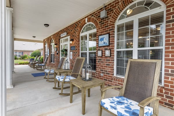 A welcoming porch with cushioned chairs set against a brick building with large windows.