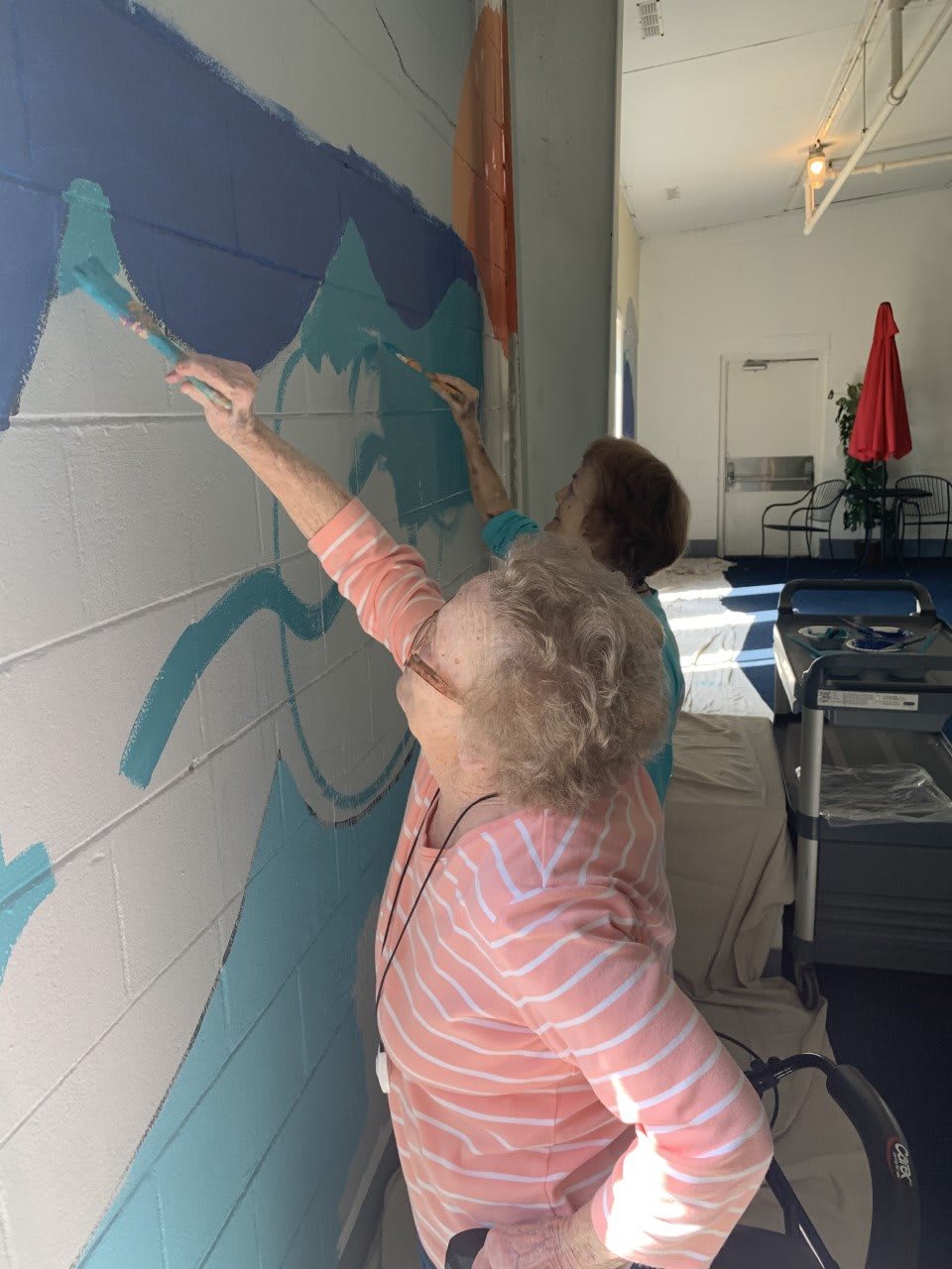 Two individuals collaborate on painting a mural on a wall.