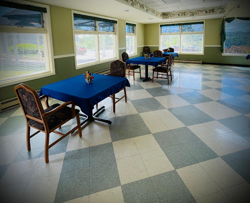 An empty dining room featuring blue tables and chairs, with large windows allowing natural light.