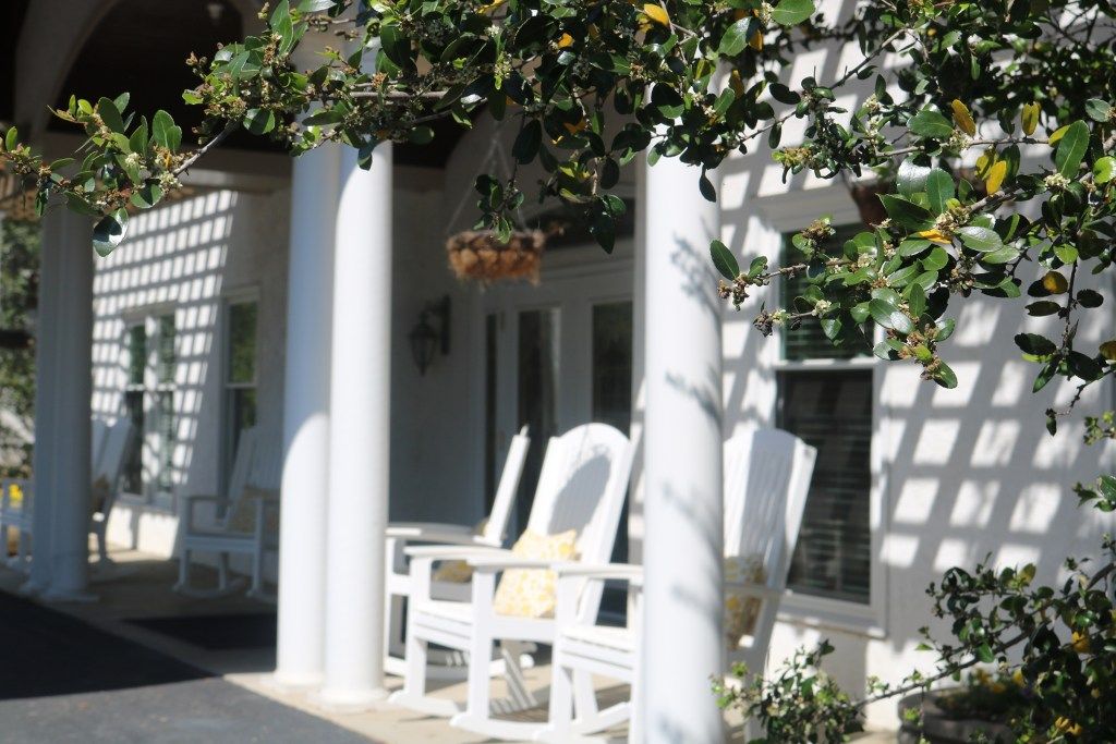 A sunny porch featuring white rocking chairs and columns, complemented by hanging plants.