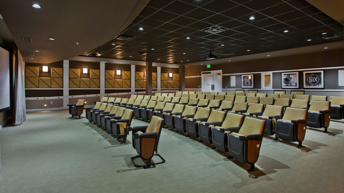 An empty auditorium with rows of comfortable seating and a modest stage area.