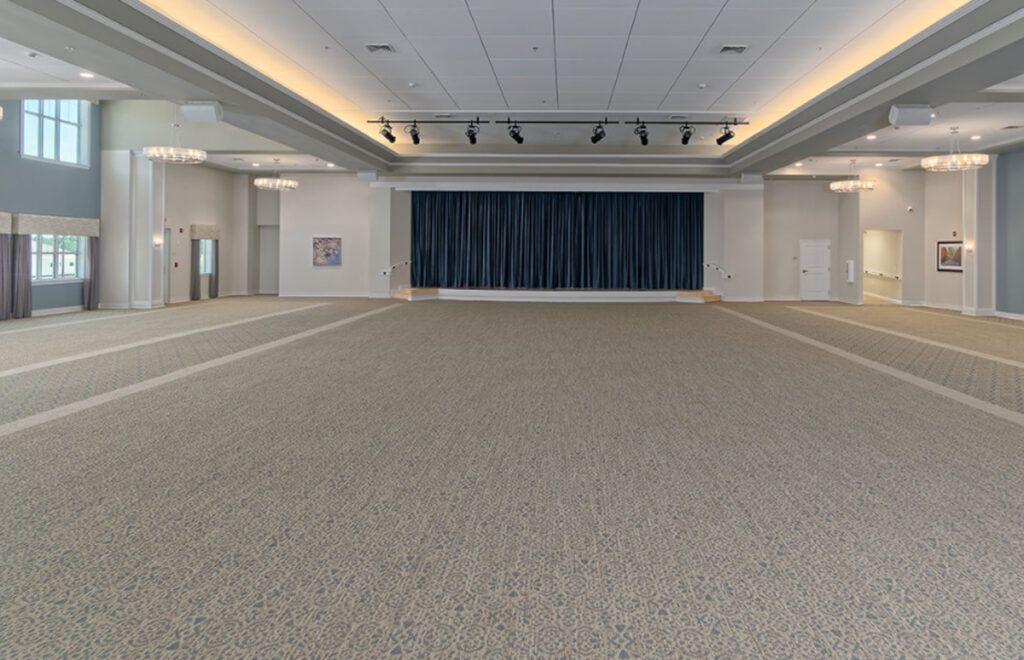 An empty conference hall with carpeted flooring and a stage with curtains.