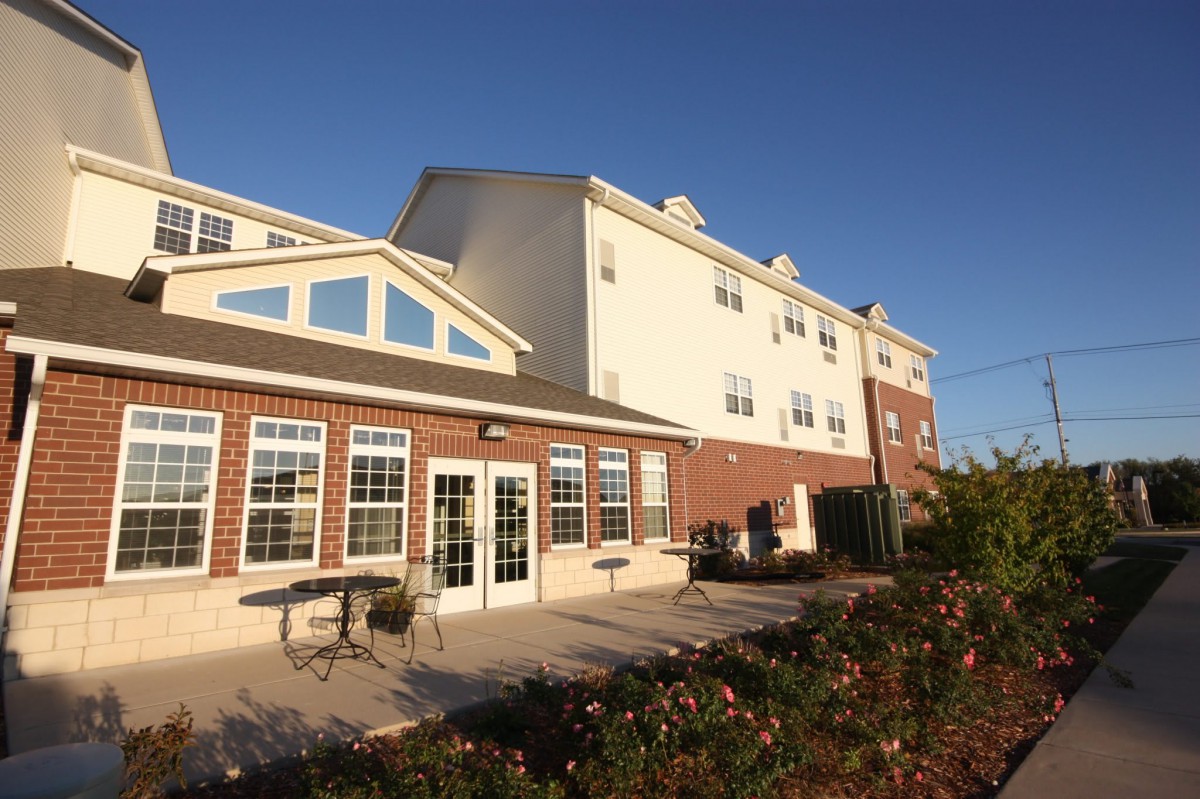 A bright exterior view of a building with large windows and outdoor seating bathed in sunlight.