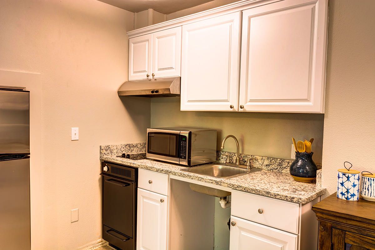 A modern kitchen with white cabinets and a granite countertop, featuring a microwave, sink, and dishwasher.