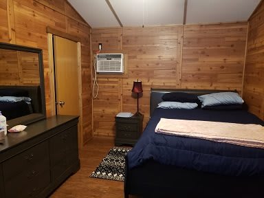 Cozy wooden bedroom with a bed, dresser, and air conditioner.