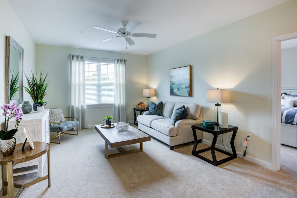 A cozy living room with a comfortable sofa, coffee table, and soft lighting from lamps, featuring a ceiling fan and wall artwork.