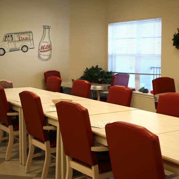 A spacious dining or meeting area with red chairs and a long table, adorned with wall art and plants.