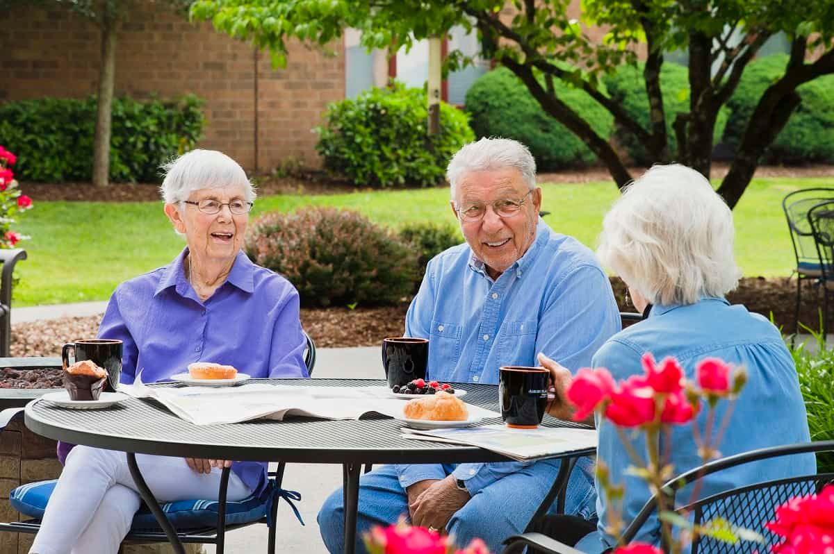 A group of seniors enjoying coffee and conversation outdoors in a garden setting.