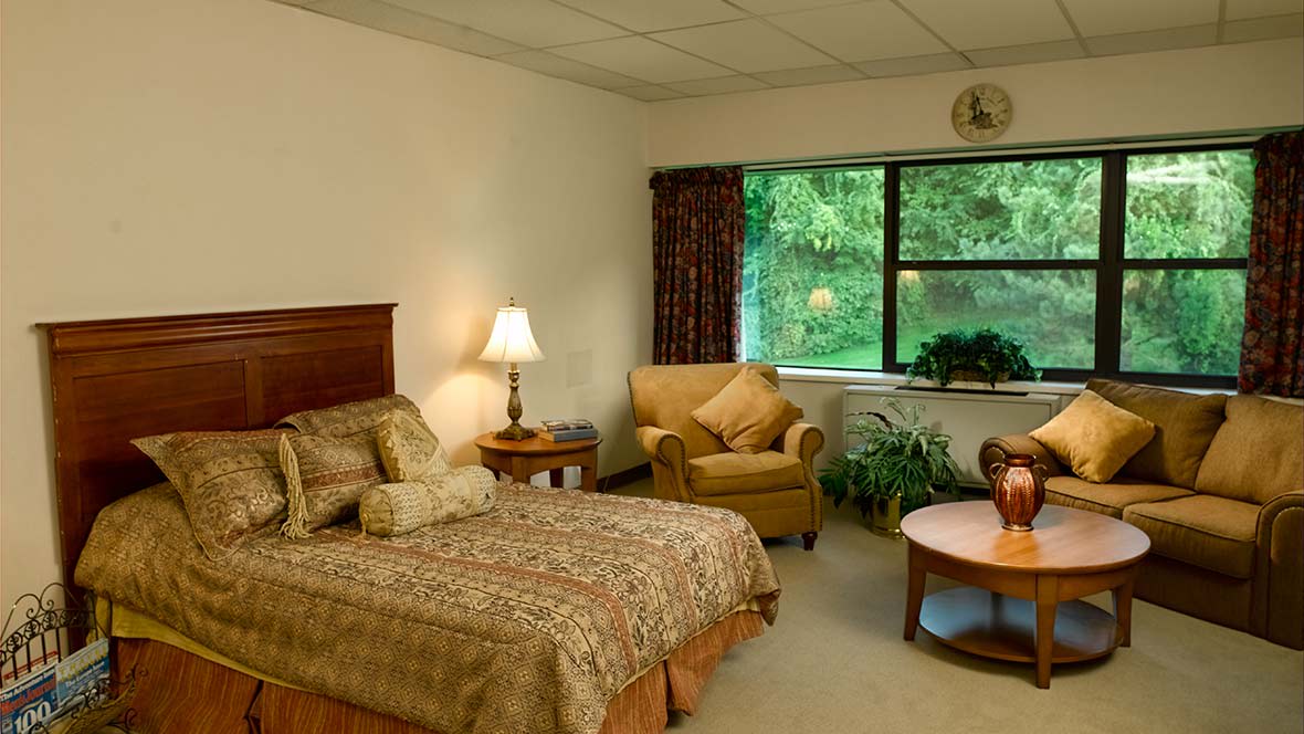 A cozy bedroom with a bed, armchair, and a view of greenery through the window.