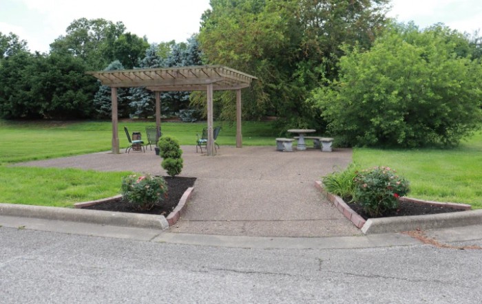 A peaceful park setting with a pergola and outdoor seating surrounded by lush greenery.