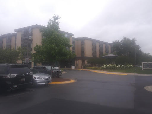 A hotel building seen on a cloudy day, featuring a parking lot and greenery.
