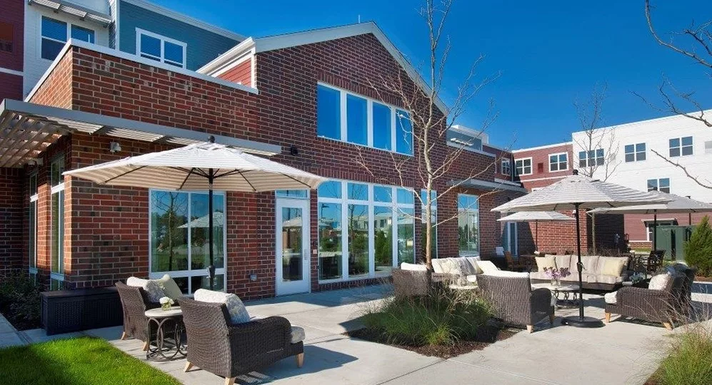 A modern brick building with a spacious patio area featuring outdoor seating and umbrellas on a sunny day.