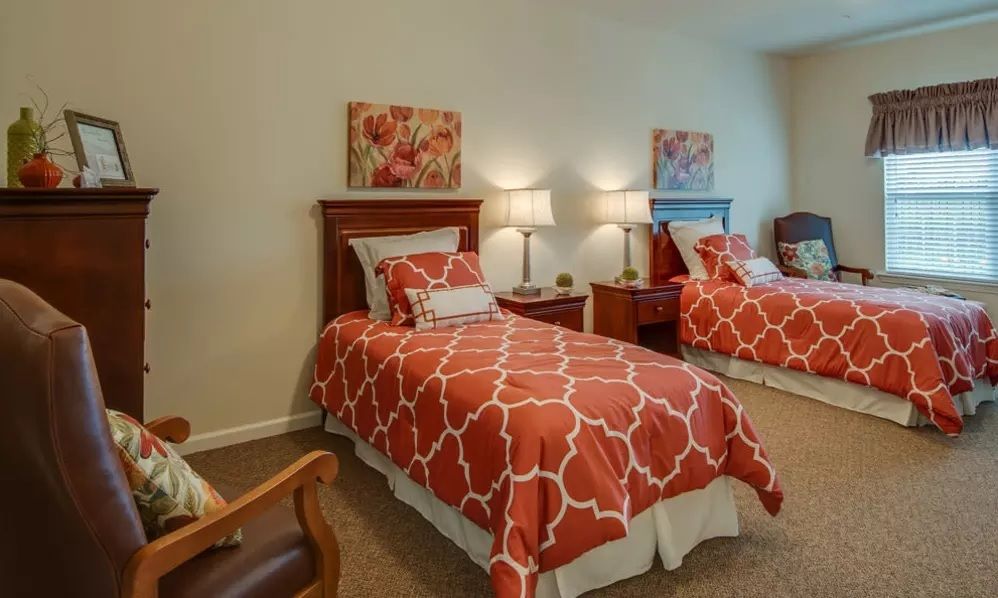 A cozy bedroom featuring two twin beds with orange patterned bedspreads, complemented by bedside tables and lamps, along with decorative wall art.