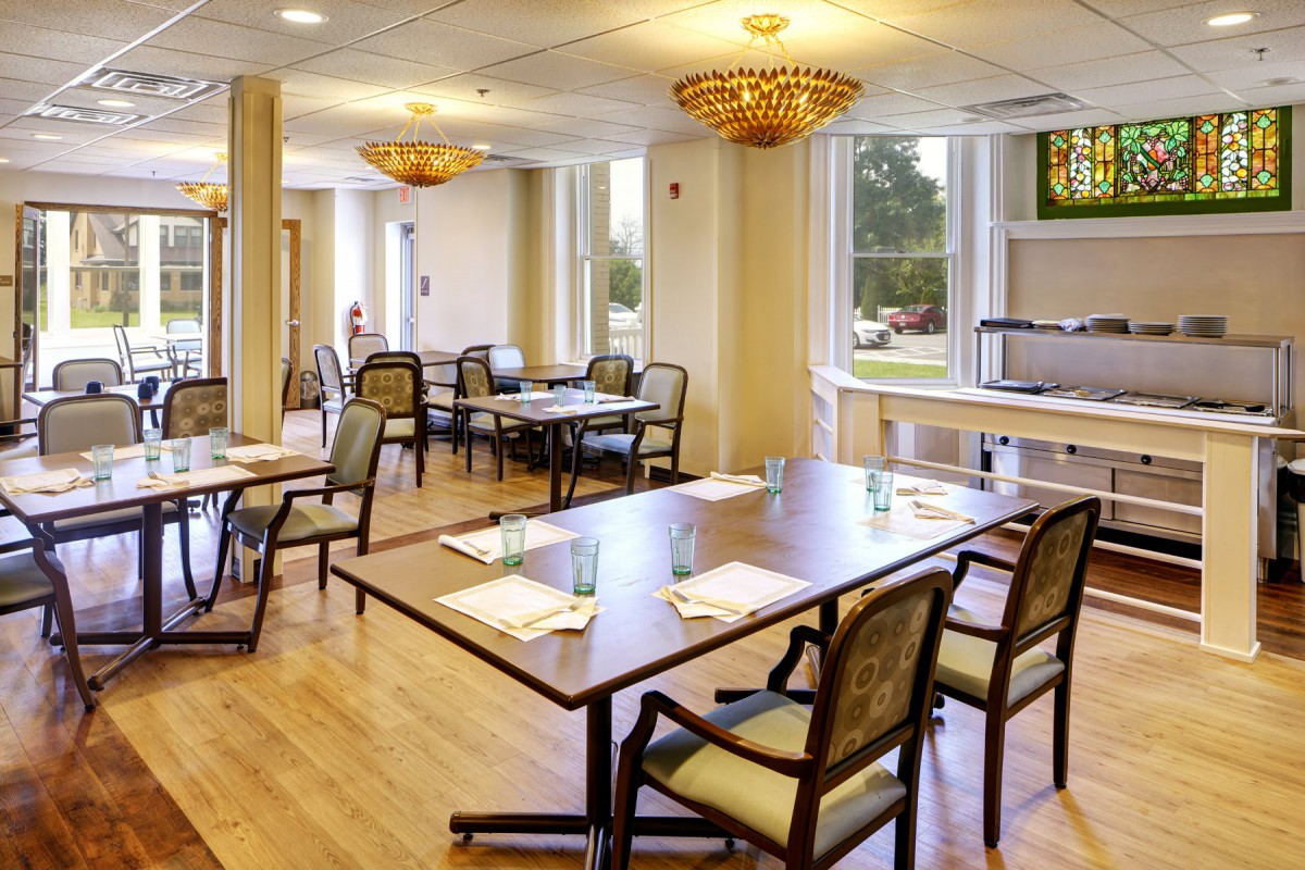 A well-lit dining room with neatly arranged tables and chairs, adorned with elegant chandeliers.