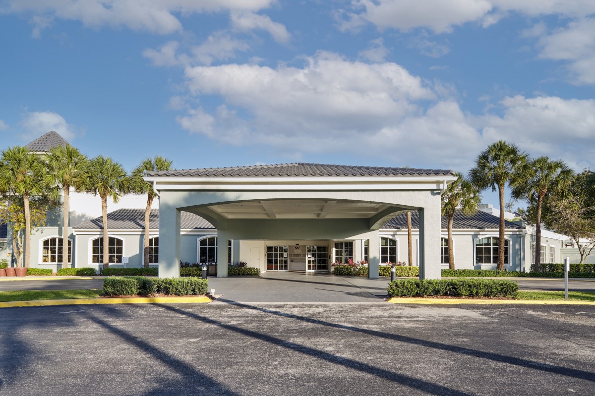 A modern building entrance with palm trees and a partly cloudy sky.
