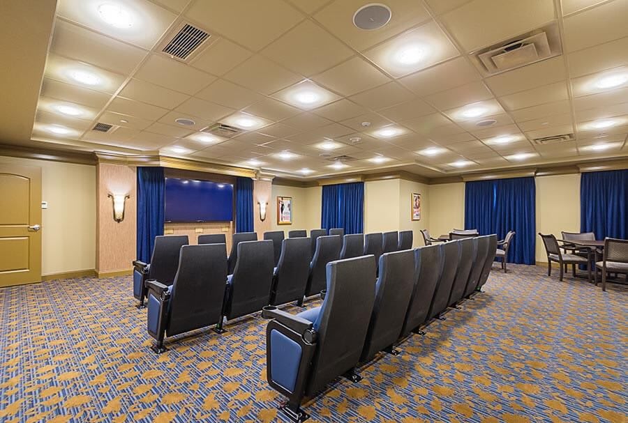 A well-lit theater-style room with rows of comfortable seating facing a projector screen.