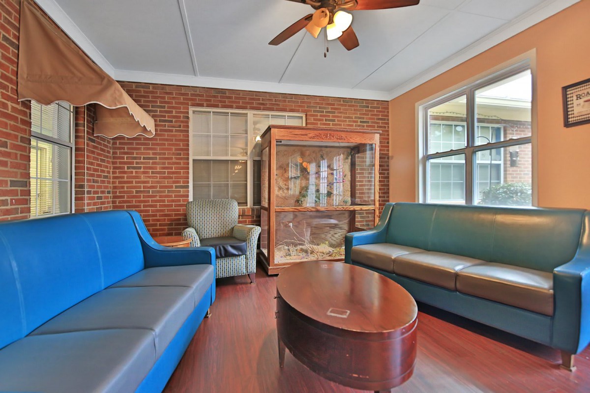 A cozy living room with sofas, a chair, and a coffee table, featuring a ceiling fan and windows.