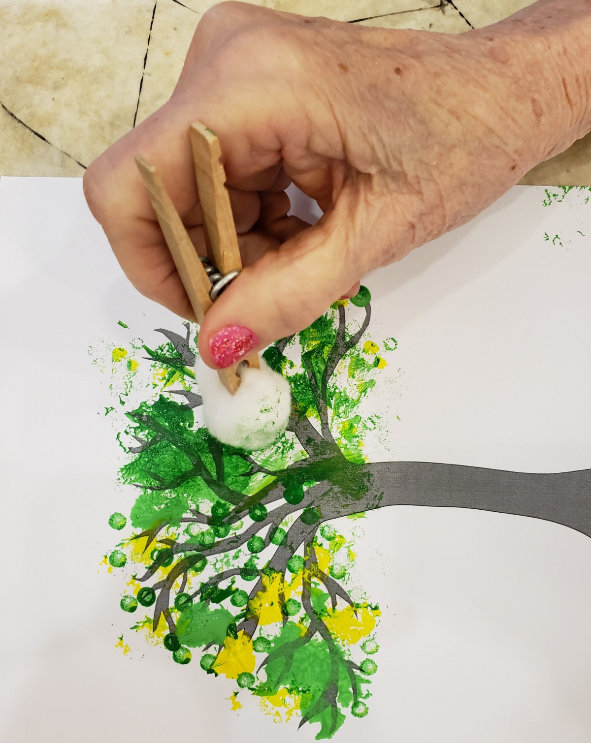 A hand using a paintbrush to create a colorful tree artwork.