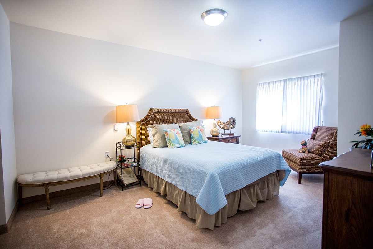A cozy bedroom featuring a bed with blue bedding, nightstands with lamps, and a window letting in natural light.