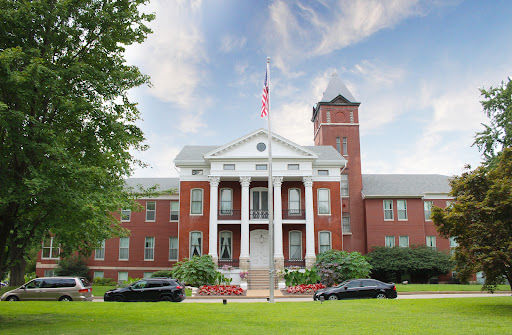 A historic building featuring classic architecture, flanked by well-maintained landscaping and parked cars.