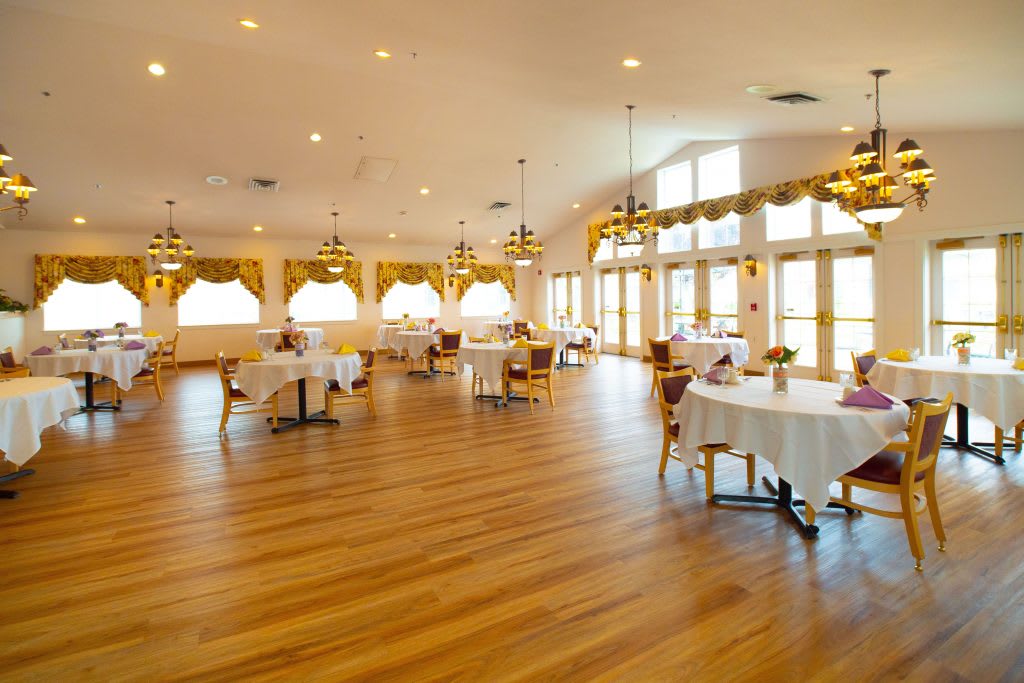 An elegant event hall with wooden flooring, decorated with tables and chairs under soft natural lighting.