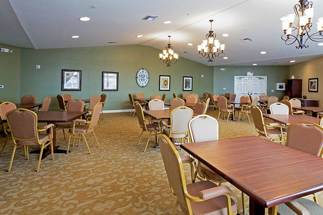 A spacious dining area with multiple tables and chairs, illuminated by chandeliers.