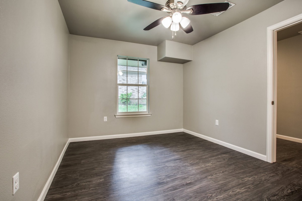 An empty room featuring hardwood flooring, a ceiling fan with lights, and a single window.