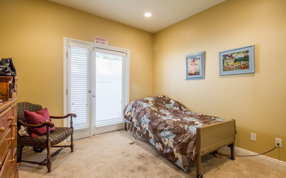 A cozy bedroom with a single bed, artwork on the walls, and a chair beside the window.