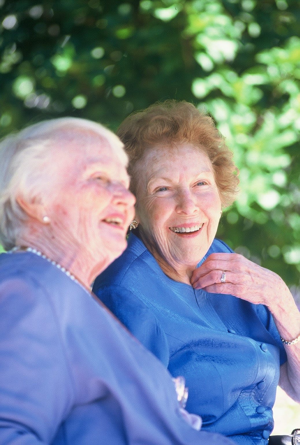 Two elderly women enjoying a moment of laughter together outdoors.