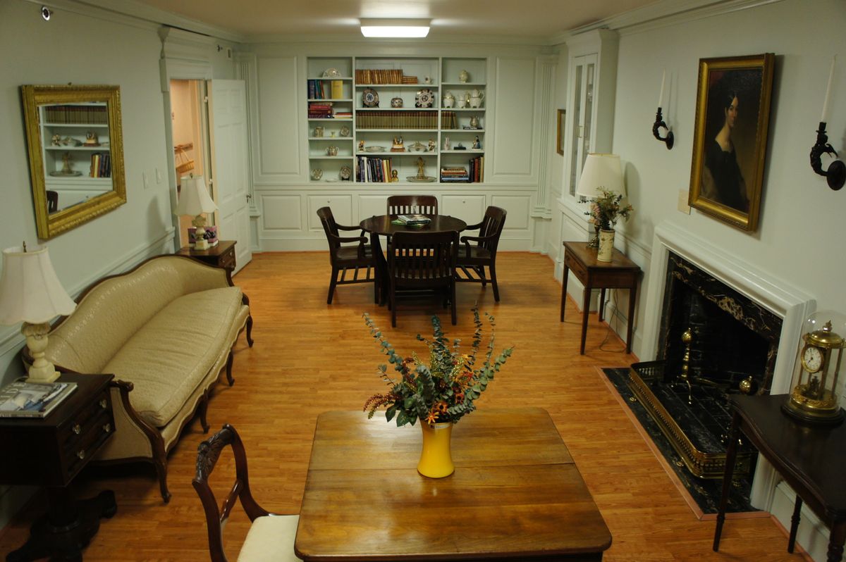 A cozy living room with a dining area, featuring classic wooden furniture and a bookshelf, enhanced by a fireplace.