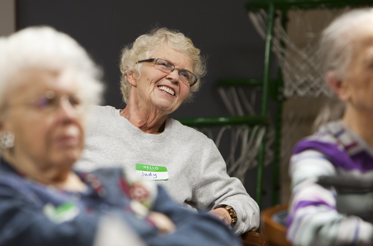 An elderly woman smiling during a casual indoor gathering.