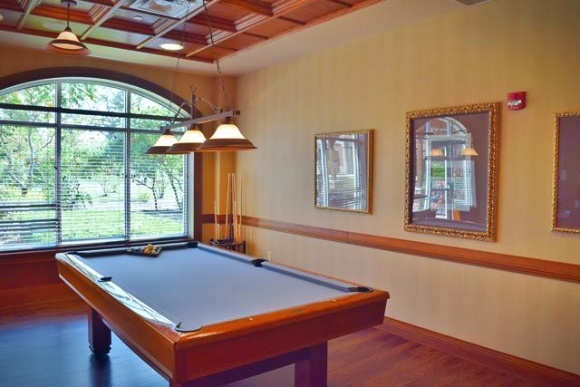 A cozy billiards room featuring a pool table, hanging lights, and large windows.