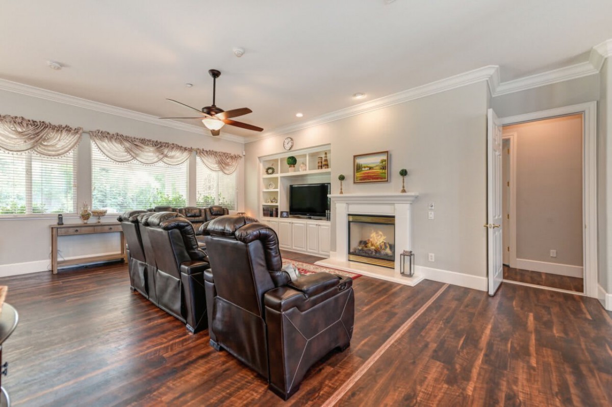 A cozy living room with leather recliners facing a fireplace and television, featuring wooden floors and a ceiling fan.