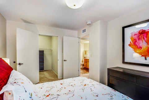 A cozy bedroom featuring a bed with patterned bedding, an open closet, and modern furniture.
