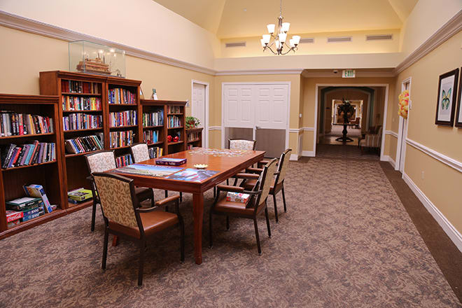 A cozy library space with a central table surrounded by chairs and bookshelves lining the walls.